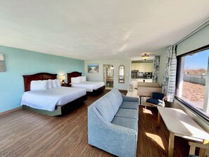 A hotel room with two beds, a sofa, a dining table, and a view of the beach.