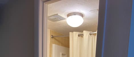 Une salle de bain comprenant des toilettes, une douche avec un rideau, un téléphone fixé au mur et un sol carrelé.