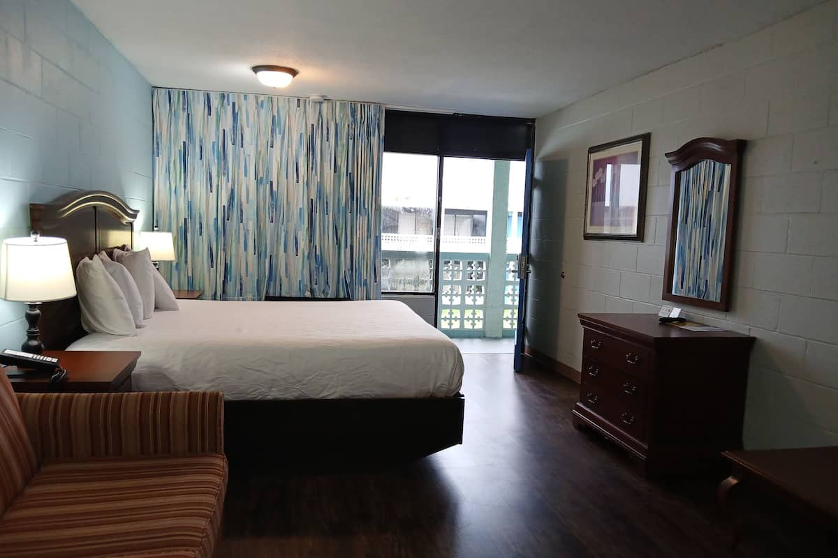 Habitación de hotel con cama, lámparas de noche, cómoda, una silla y vistas al exterior.
