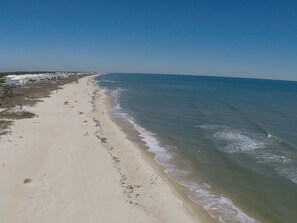 A beach with a long stretch of sand, a few umbrellas, and a clear view of the ocean.