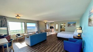 A hotel room with a large bed, a desk with a chair, a sofa, and a balcony with a view of the sea. - Buccaneer Inn (St. George Island)