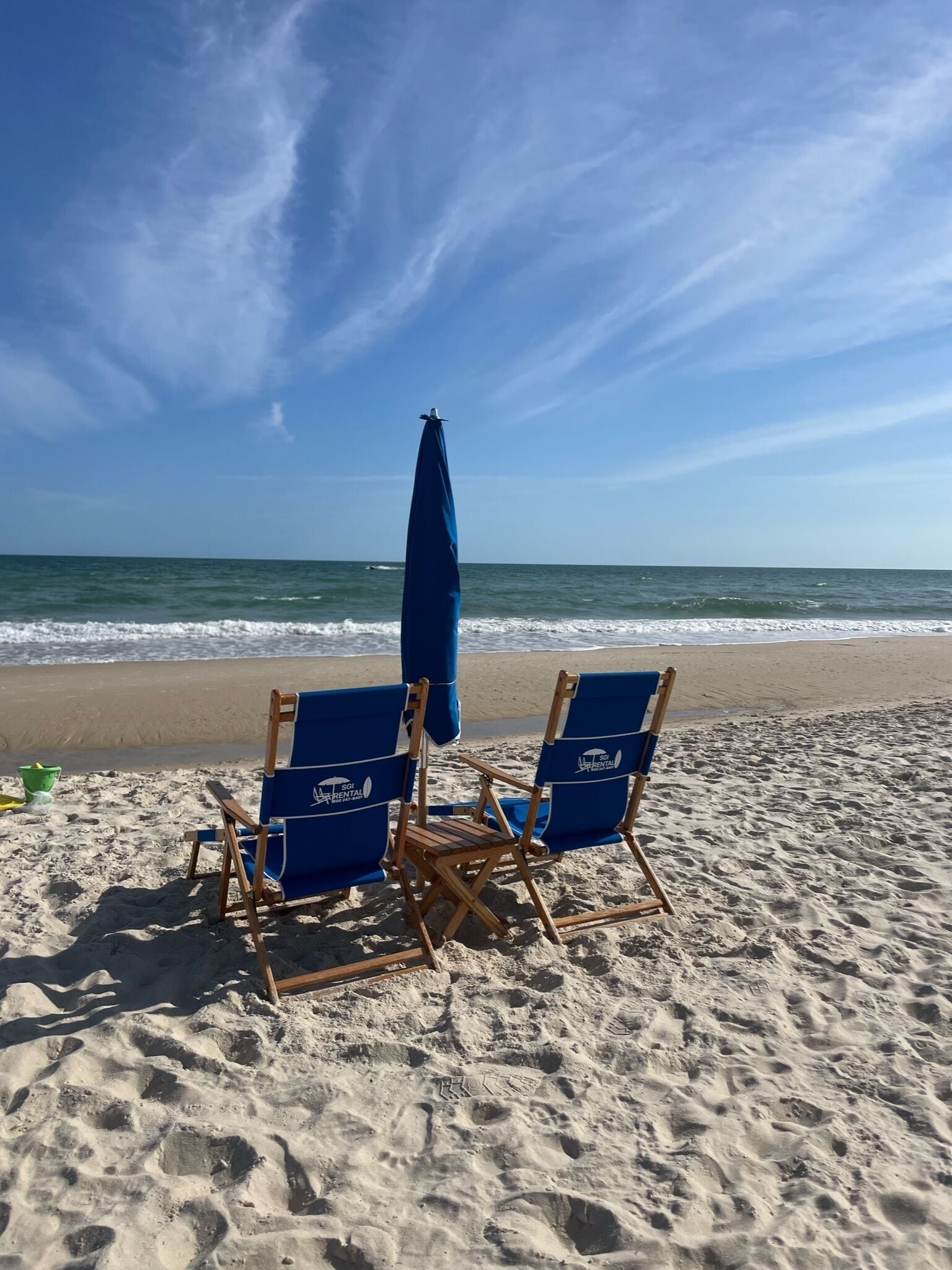 Duas cadeiras de praia azuis com um guarda-sol do mesmo tom numa praia arenosa.