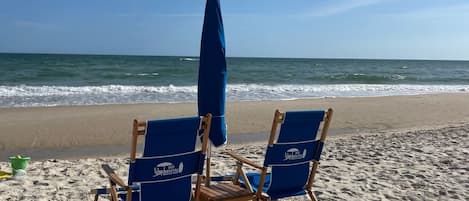 Two blue beach chairs with a matching umbrella on a sandy beach.