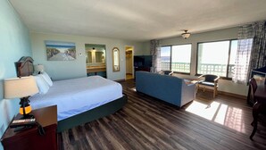 A hotel room with a bed, a sofa, a TV, a balcony with a view, and a bathroom. - Buccaneer Inn (St. George Island)
