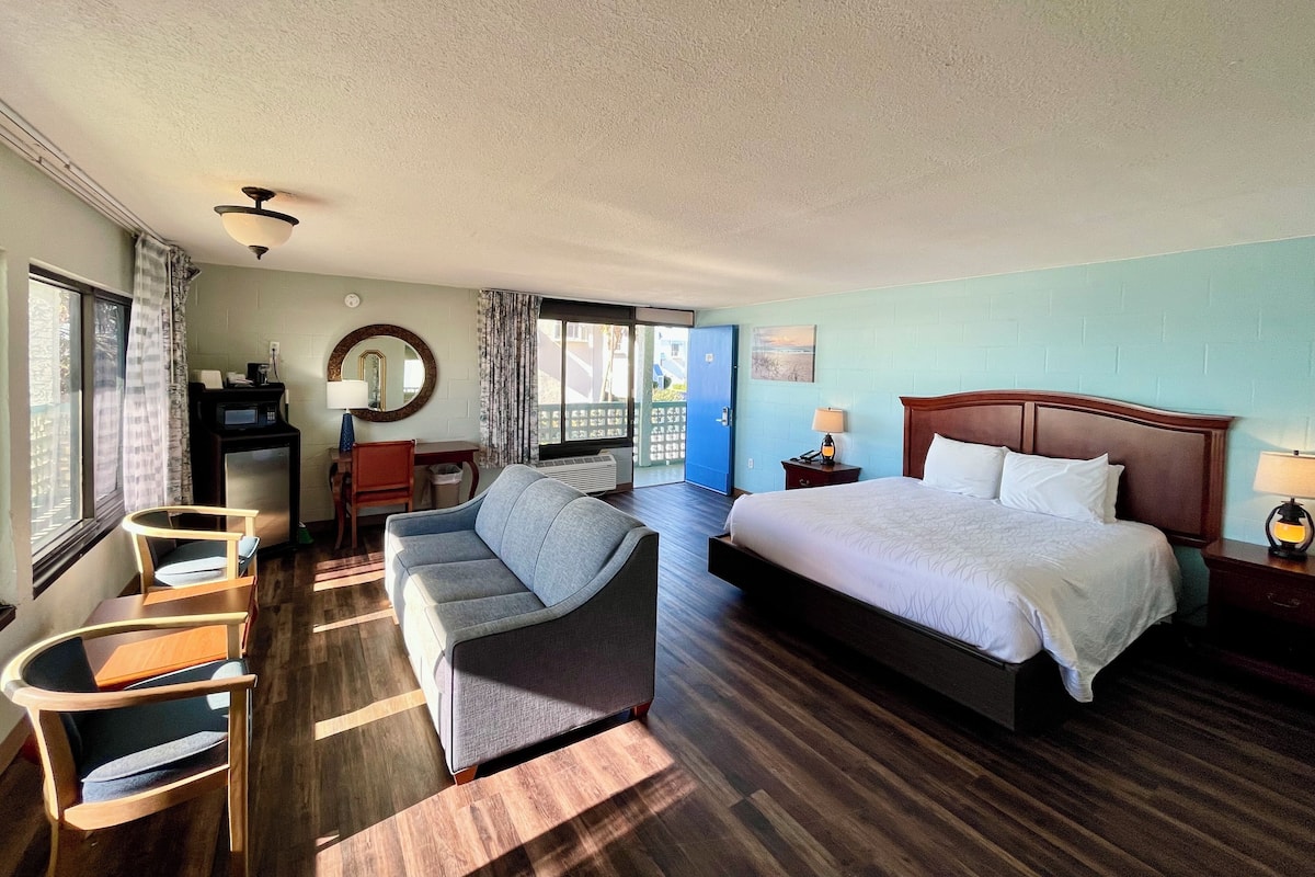 Habitación de hotel con cama, escritorio, silla, sofá, microondas, calefacción y ventana con cortinas.