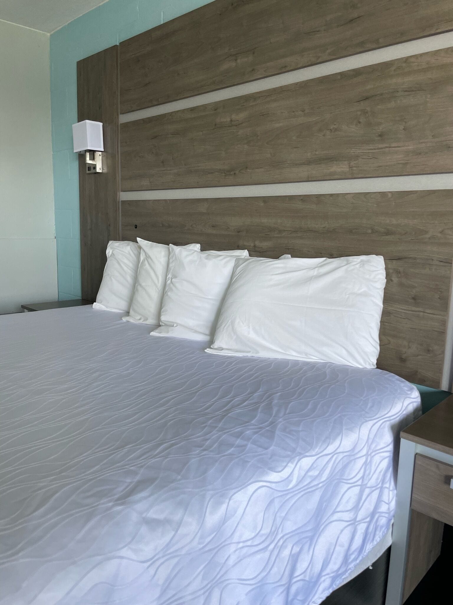 Una habitación de hotel con una cama grande, ropa de cama blanca, un cabecero de madera y una mesita de noche.