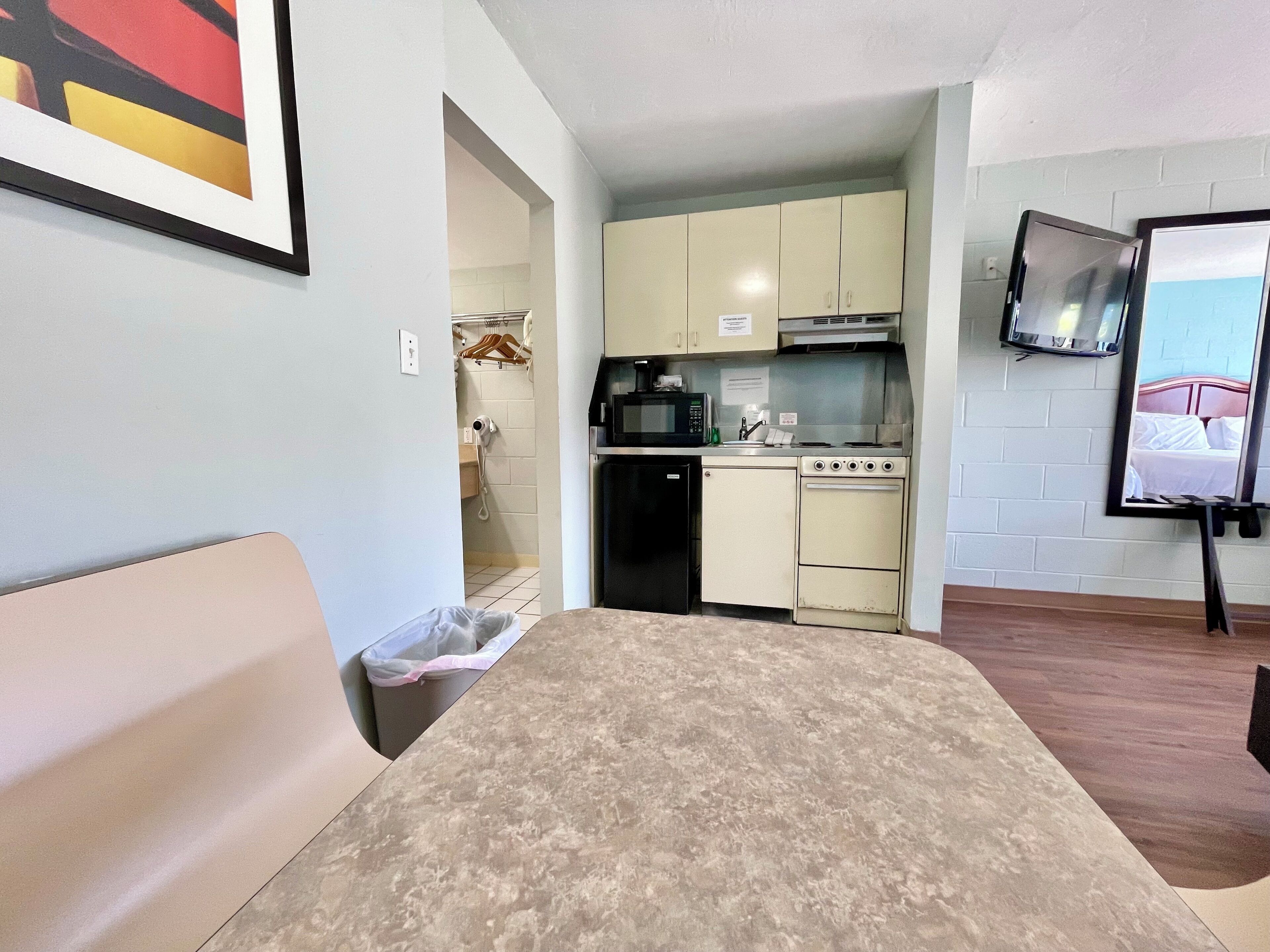 A compact kitchen with a microwave, stove, and sink. There is a small trash bin and a framed picture on the wall.