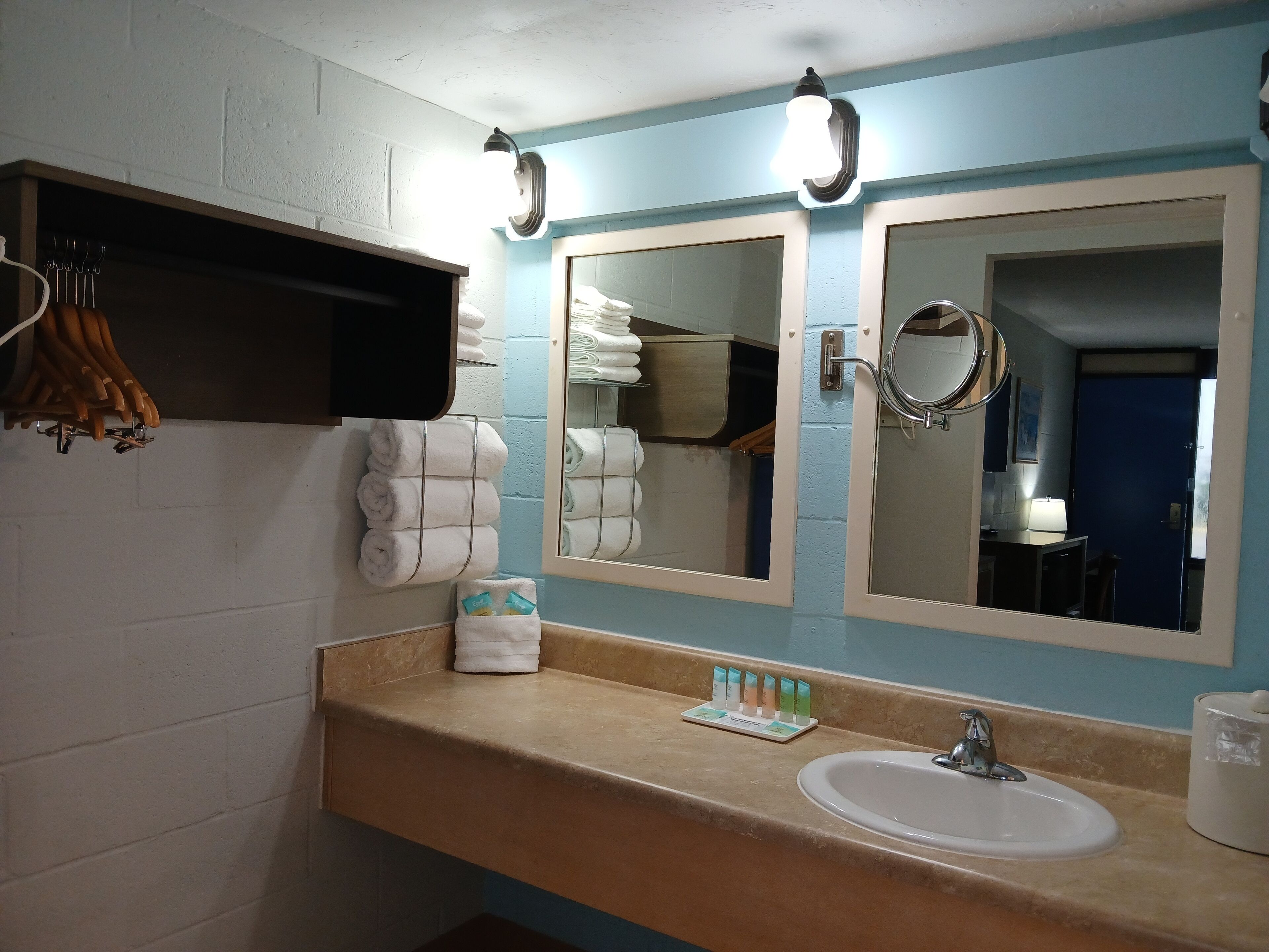Un baño con lavamanos, dos espejos, un perchero para toallas y un estante con artículos de aseo.