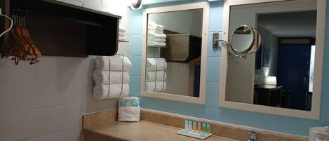 Un baño con lavamanos, dos espejos, un perchero para toallas y un estante con artículos de aseo.