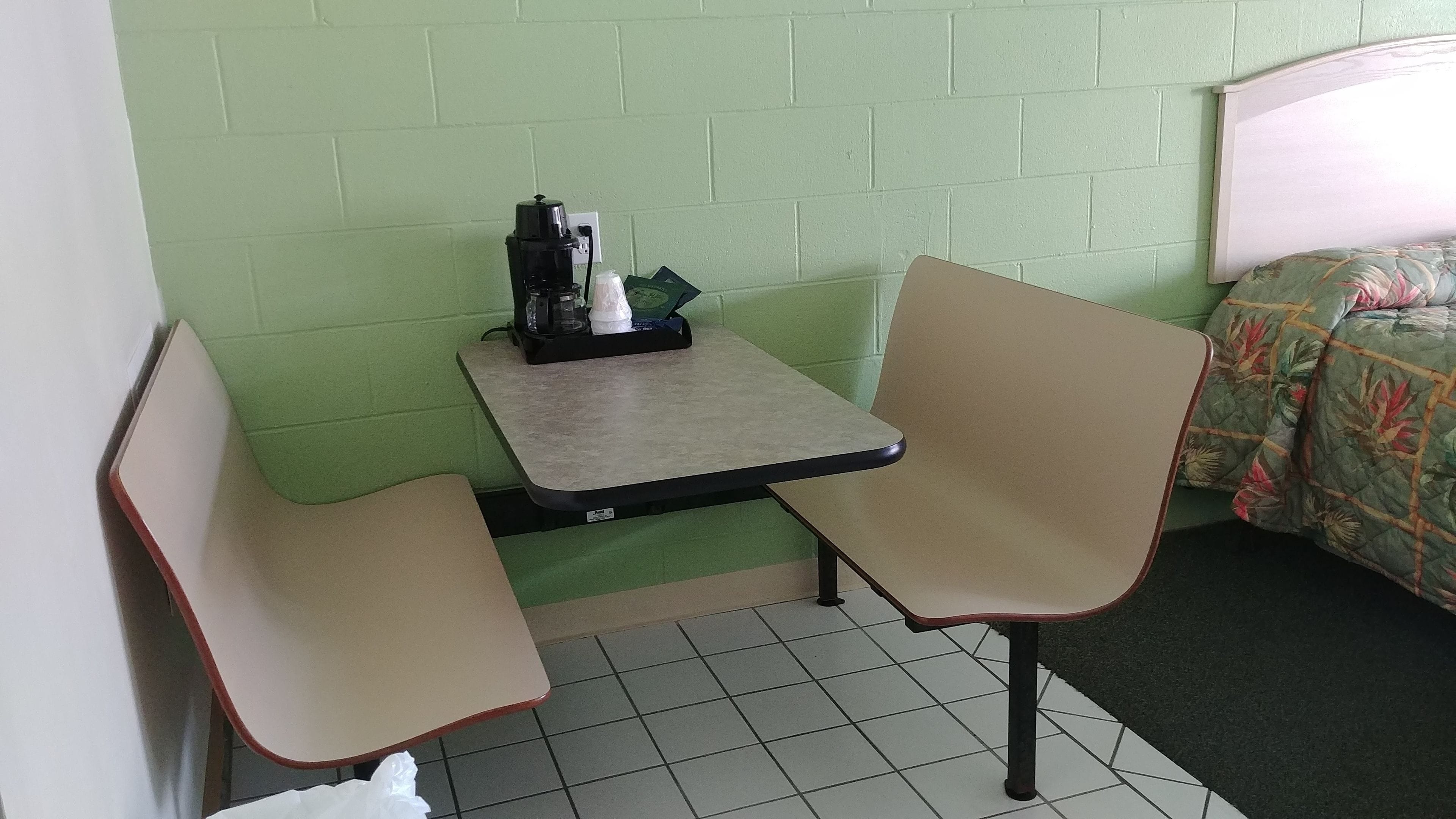 A small, private room with a single table and two chairs, a bed with floral bedding, and a green brick wall.