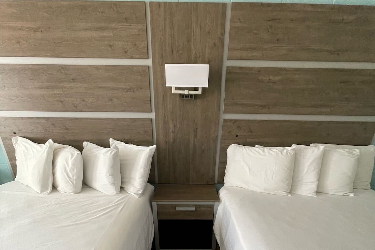 Habitación de hotel con dos camas, cabecera de madera, mesita de noche y lámpara fijada a la pared.