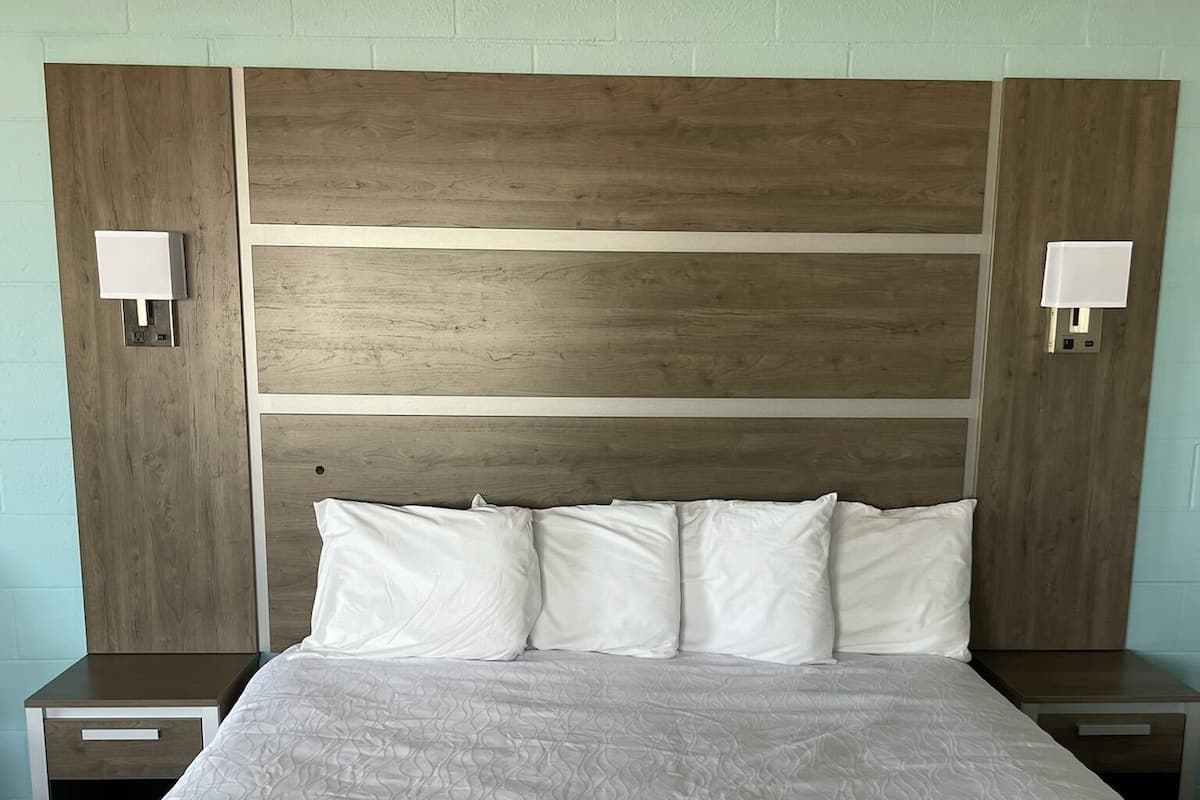 Una cama grande con cabecera de madera, dos mesitas de noche con lámparas y una pared de color claro.