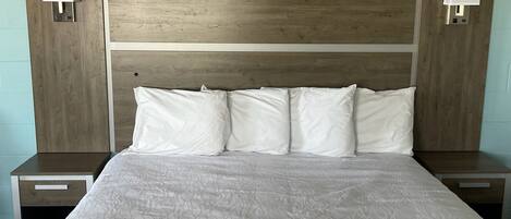 A large bed with a wooden headboard, two bedside tables with lamps, and a light-colored wall.