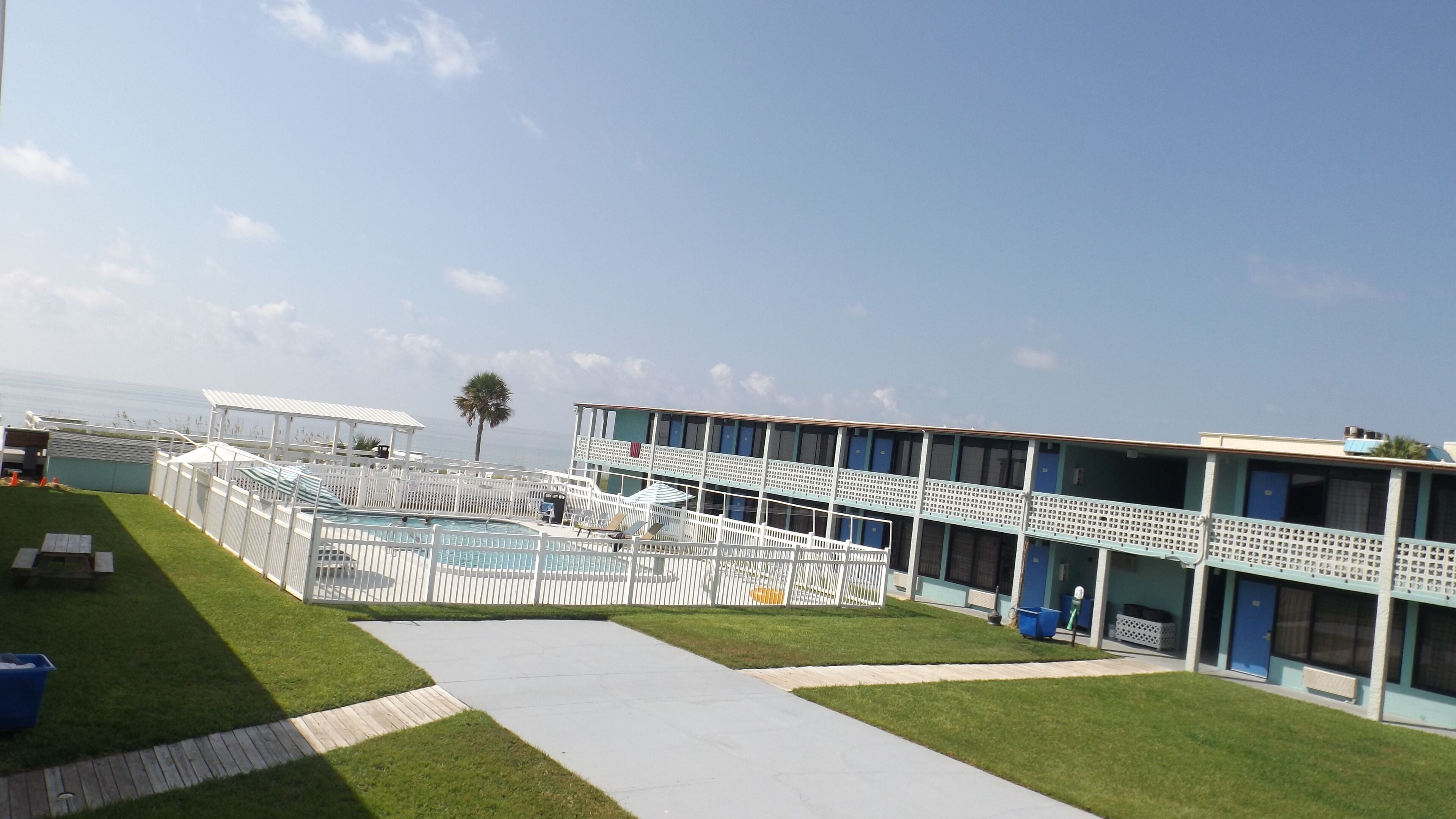 A pool area with a clear view of the ocean, a palm tree, and a building with multiple balconies.