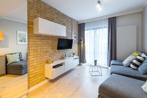 A modern living room with a brick accent wall, a flat-screen TV, a grey sofa, and a white entertainment unit.