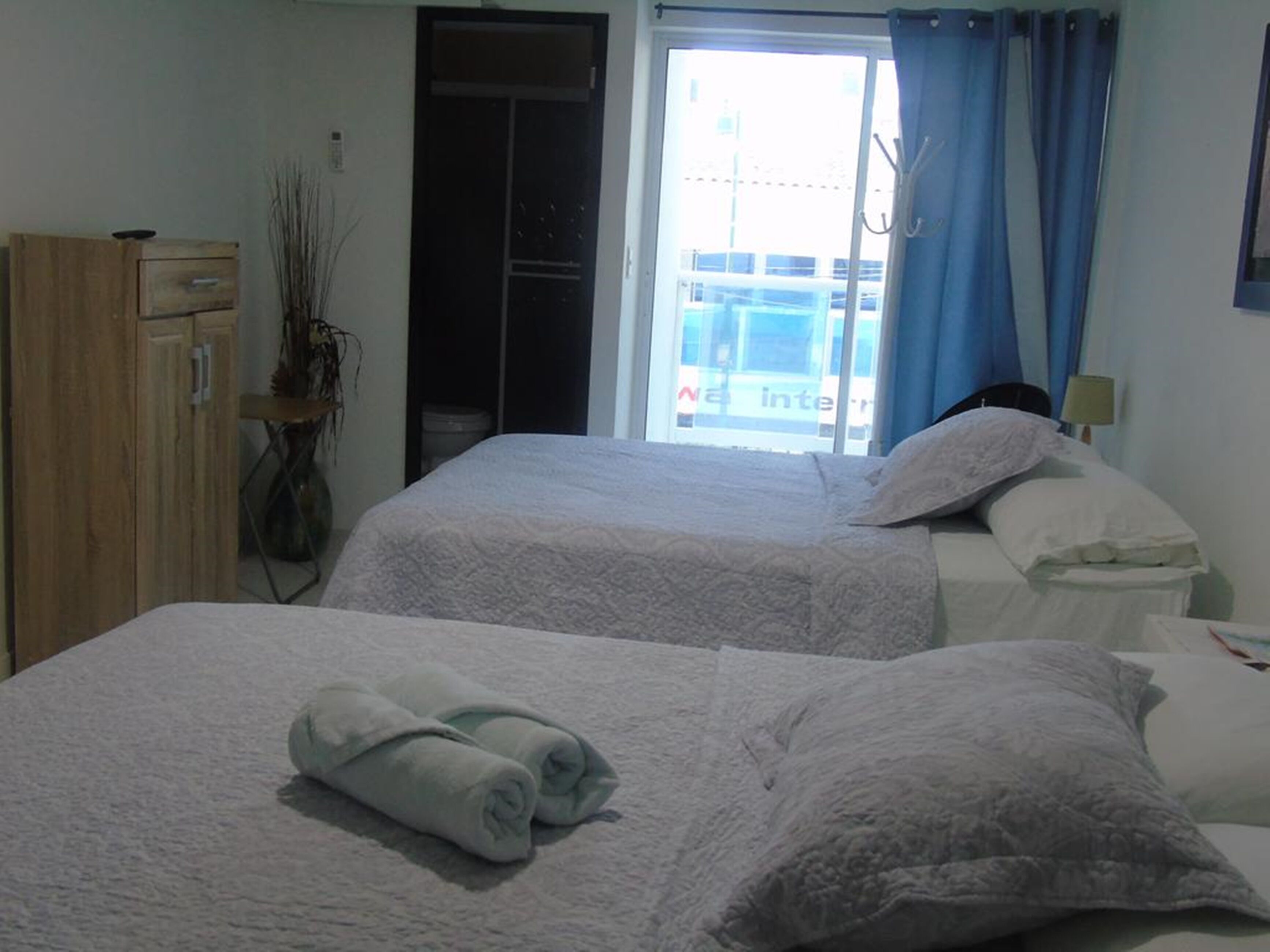A hotel room with two beds, a wardrobe, a window with curtains, and a view of the outside.