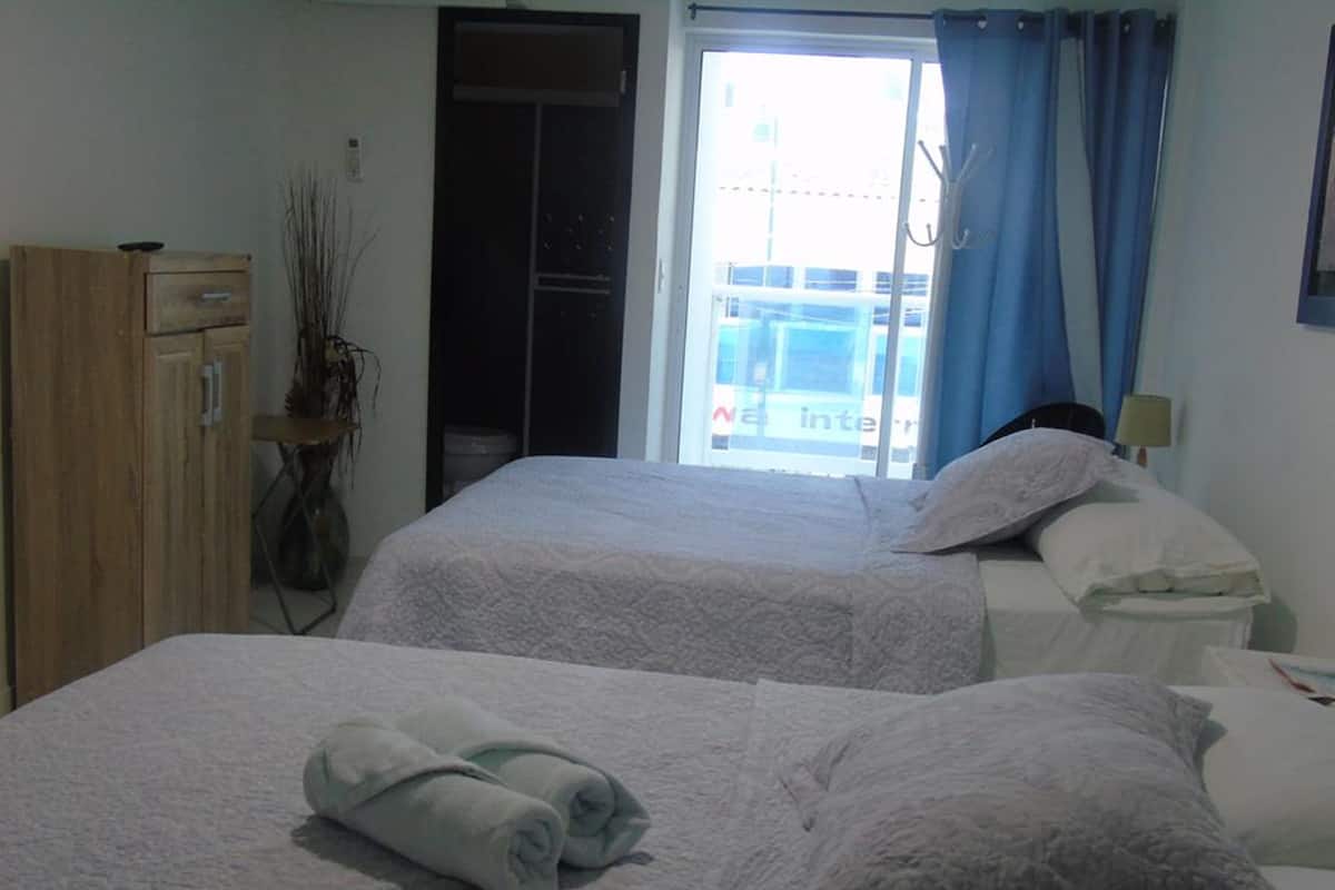 A hotel room with two beds, a wardrobe, a window with curtains, and a view of the outside.