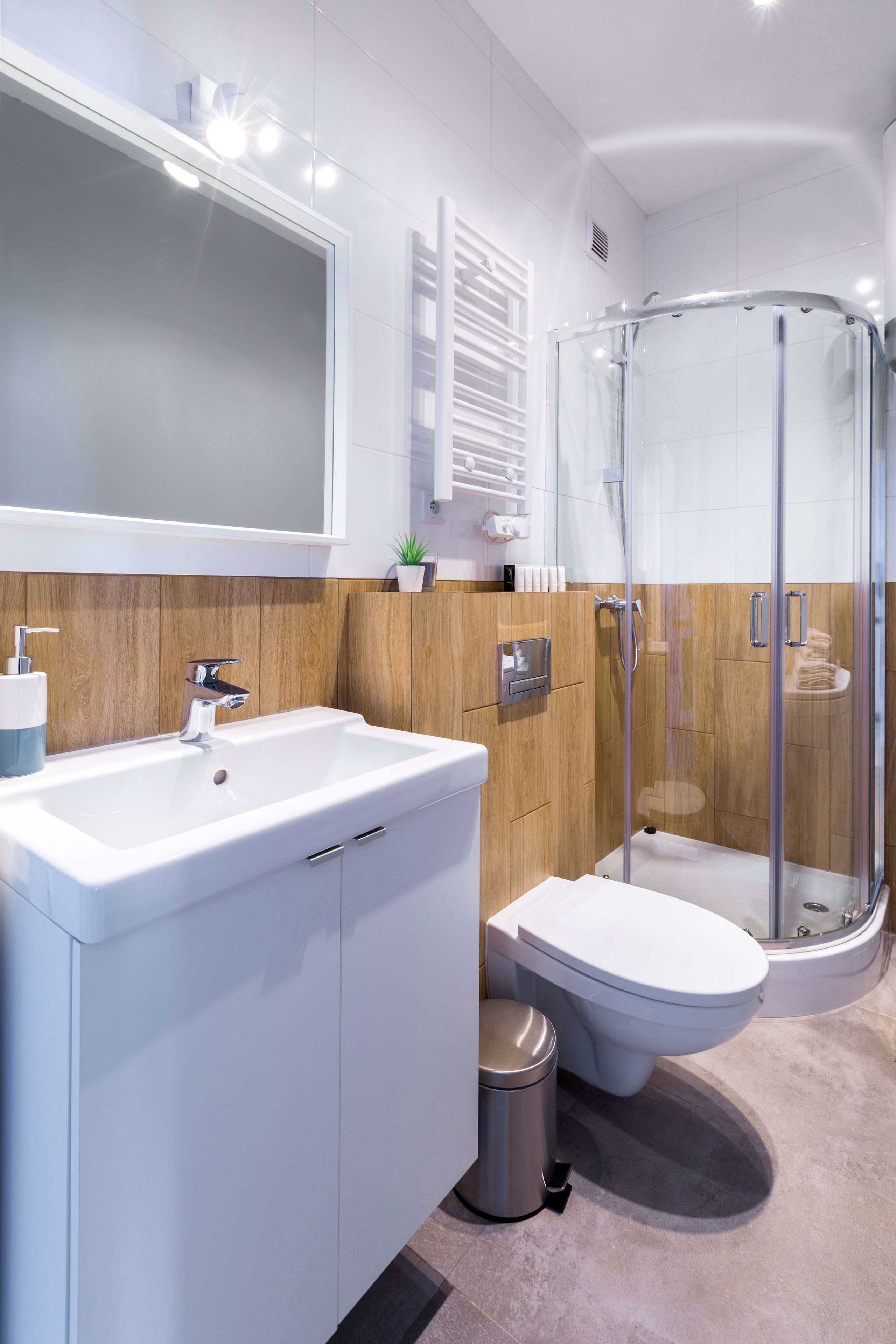 Une salle de bain moderne avec un grand miroir, un lavabo blanc et une douche à parois de verre.