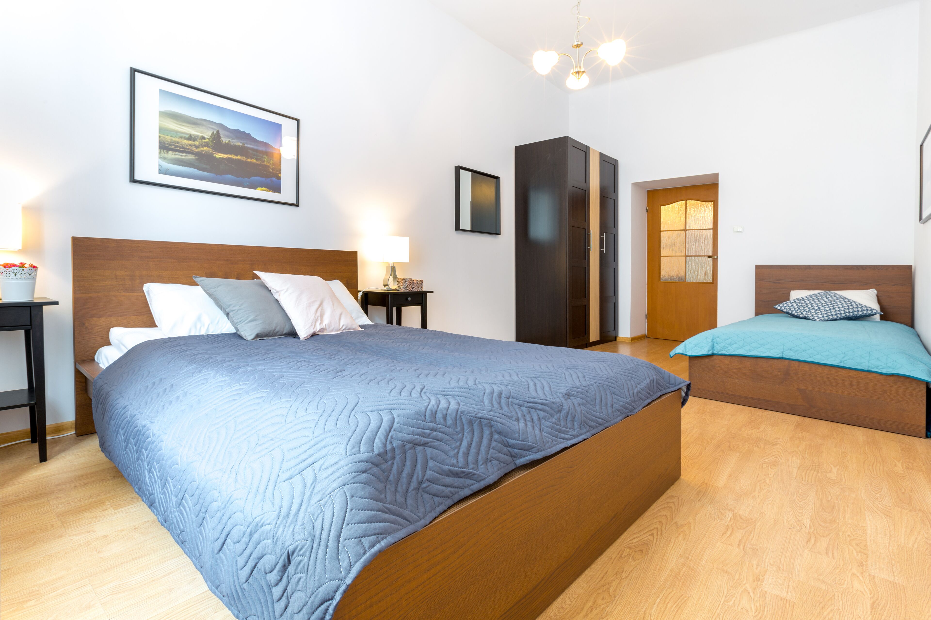 A bedroom with a large bed, a smaller bed, a wardrobe, a nightstand, a lamp, and a framed picture on the wall.