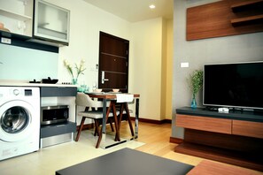 Cocina compacta con lavadora, mesa de comedor, sillas y televisor.