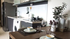 Una cocina moderna con lavadora integrada, un comedor con mesa lista para dos personas y una planta en el alféizar de la ventana.