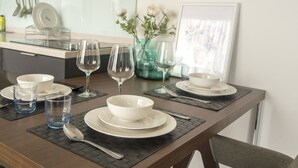 Una mesa de comedor lista con platos, tazones, vasos y cubiertos, junto con un florero con flores y un cuadro en la pared.