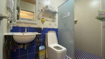 A bathroom with a white sink, toilet, and shower. There is a mirror above the sink, and a towel rack is mounted on the wall. The floor has a blue and white checkered pattern.