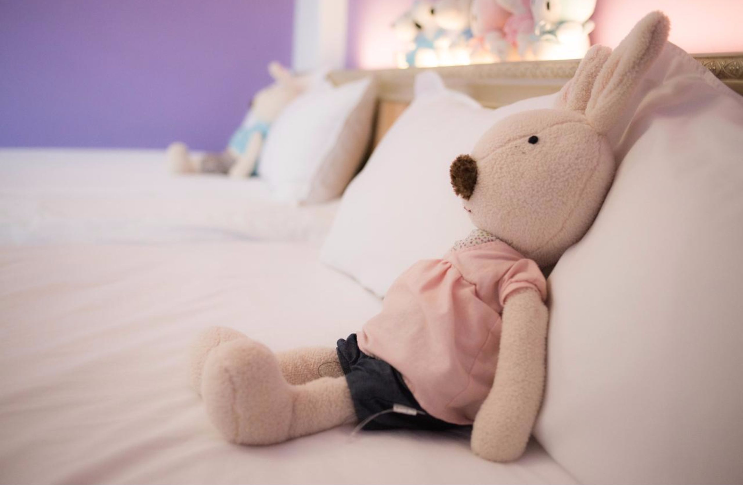 A plush toy rabbit on a bed with white bedding and pillows.