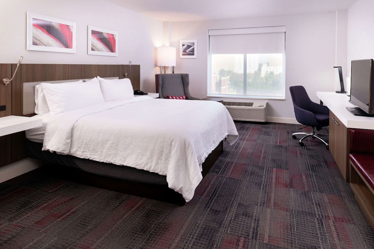 Ein Hotelzimmer mit Bett, Schreibtisch, Stuhl, Fernseher und Bildern an den Wänden.