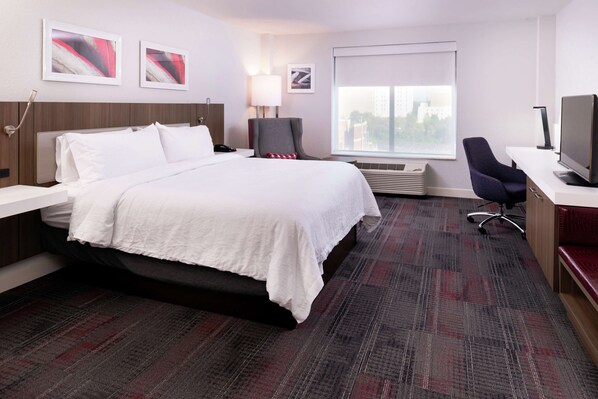 A hotel room with a bed, a desk with a computer, a chair, a TV, and a window with a city view.