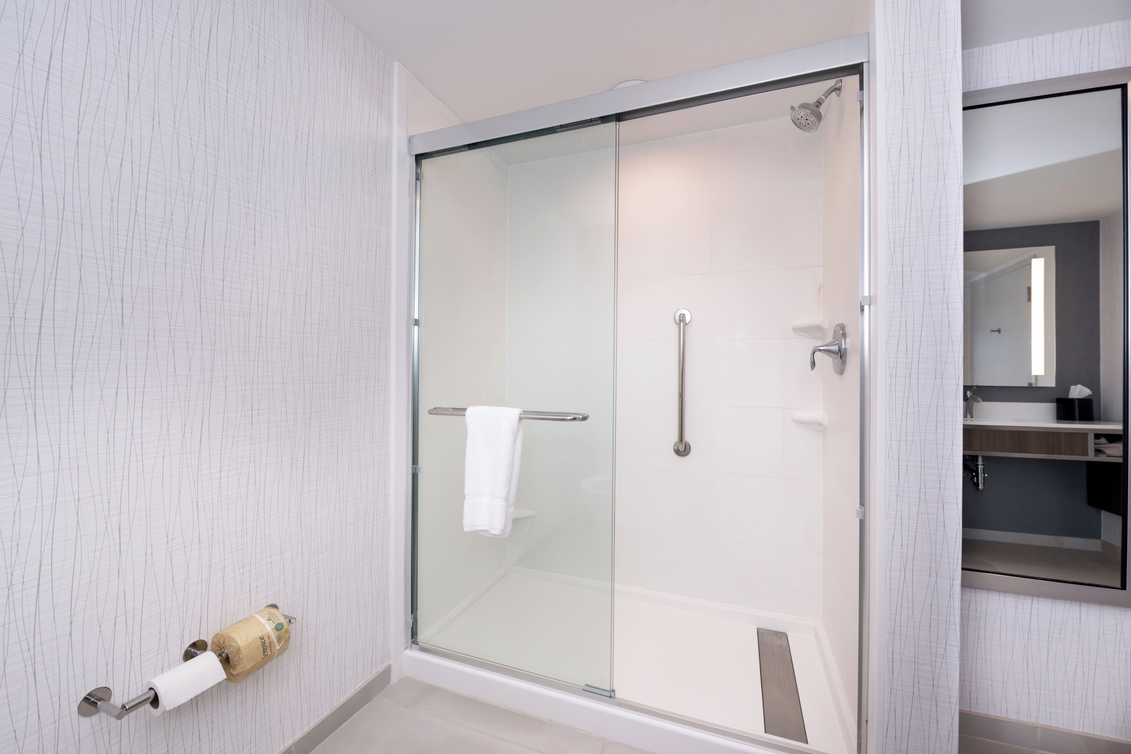 A modern bathroom with a glass shower enclosure, a towel rack, and a toilet paper holder.