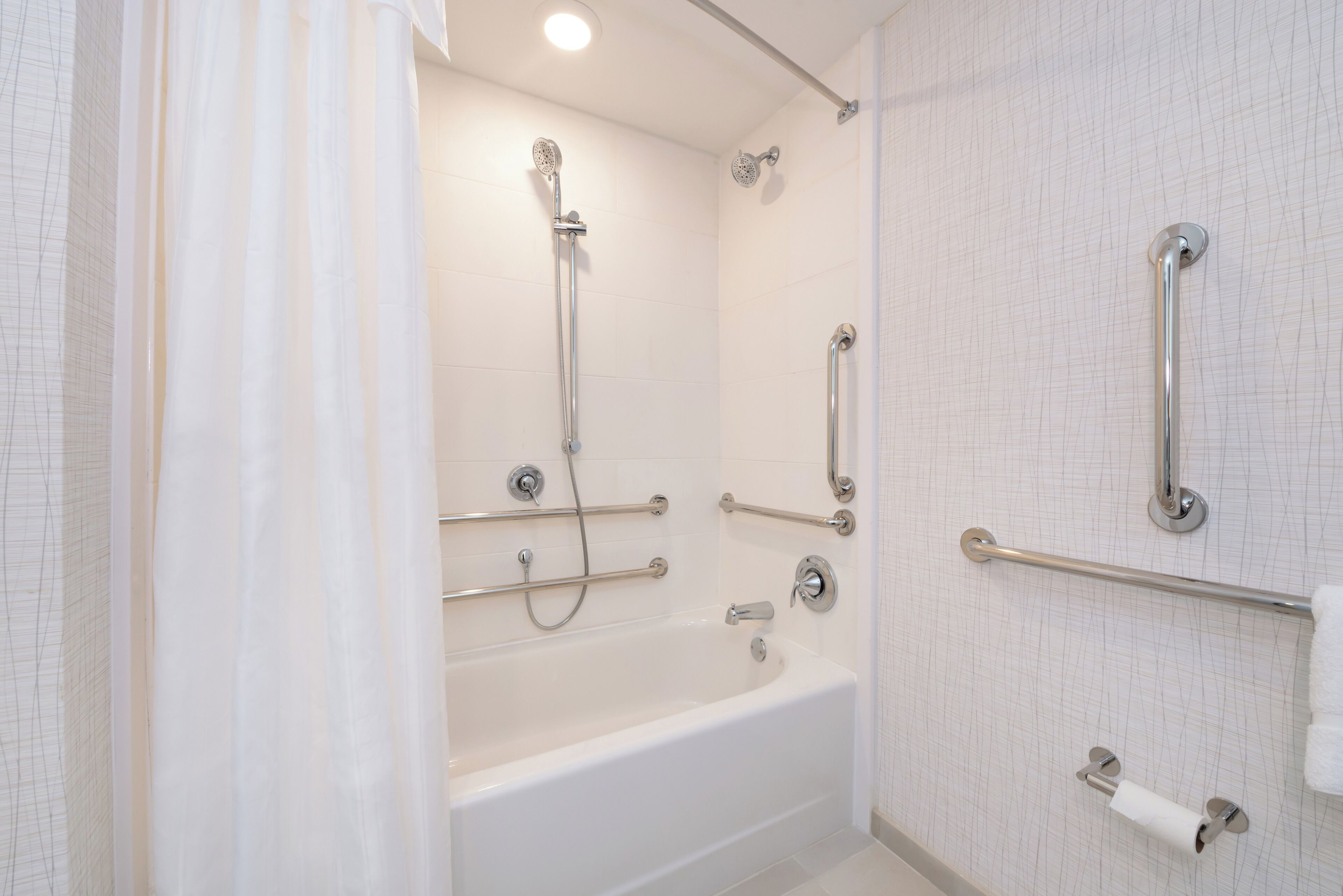 A modern bathroom with a bathtub, shower, and grab bars.
