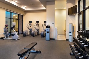 Un gimnasio con equipo de ejercicio, una banca y mancuernas.