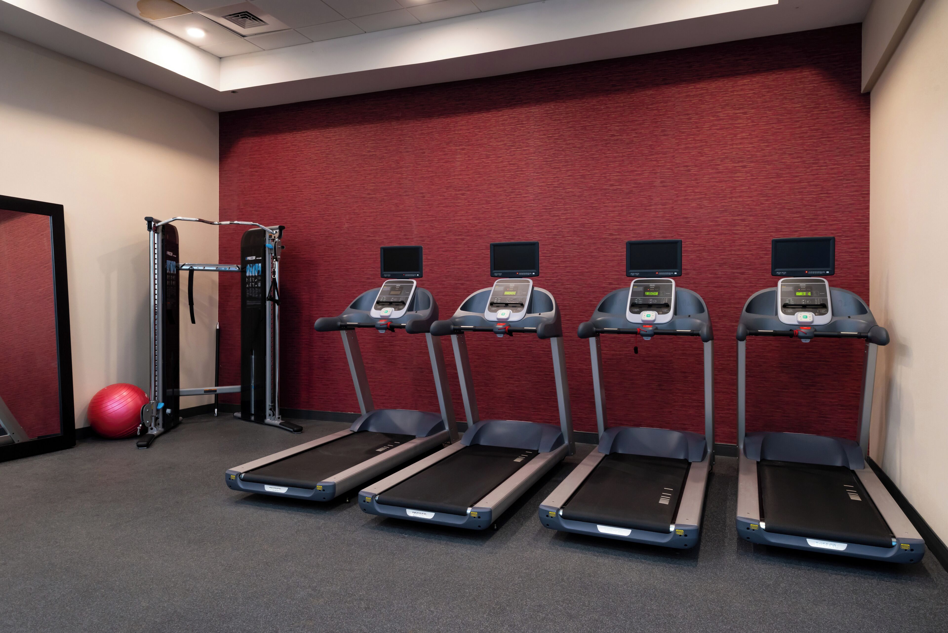 A gym with treadmills, a weight machine, and a red exercise ball.