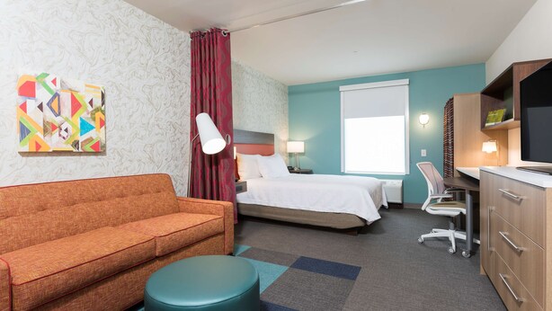 Ein Hotelzimmer mit Sofa, Bett, Schreibtisch, Stuhl und Fernseher.