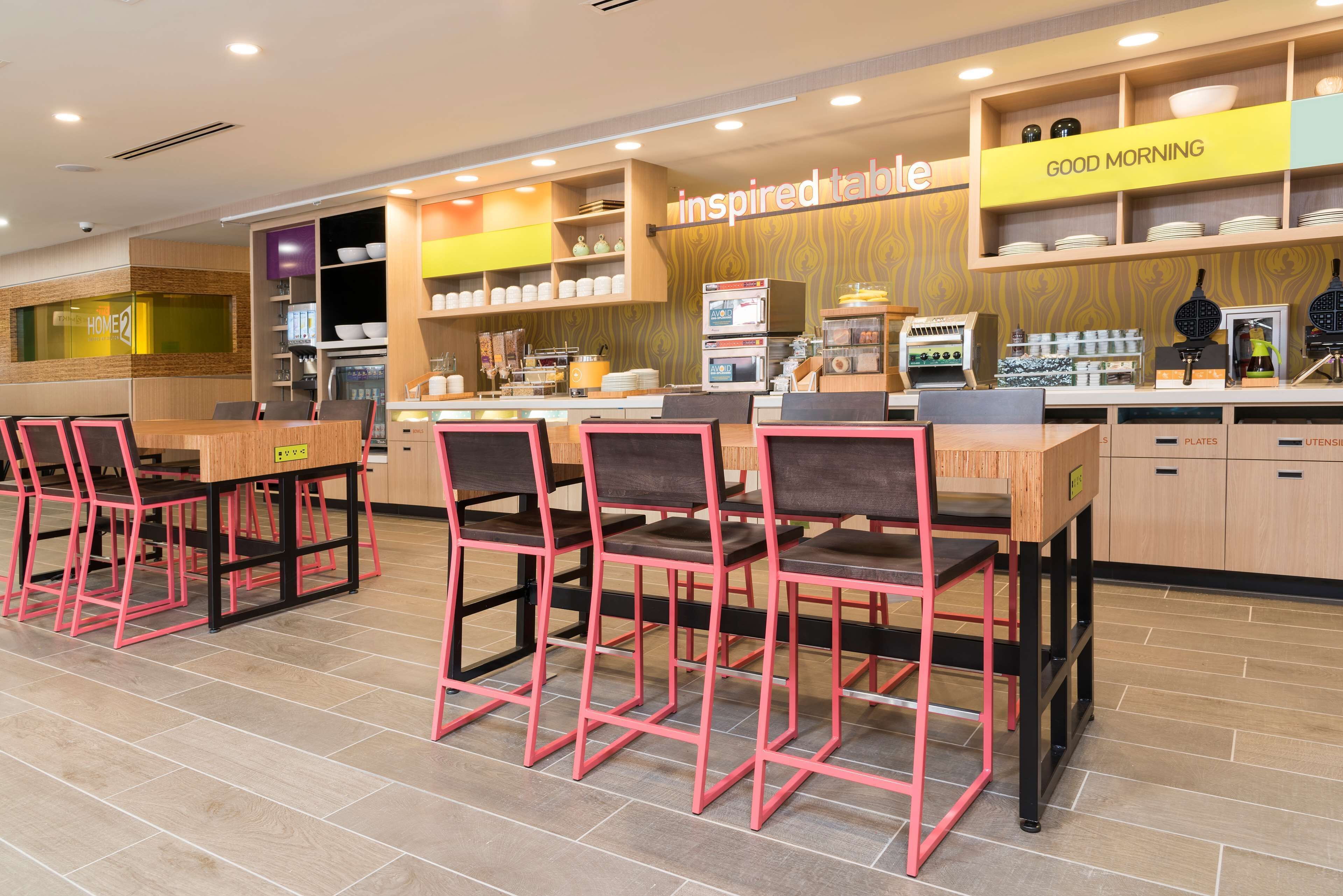 A modern cafe with a wooden counter, pink chairs, and a 'Good Morning' sign.