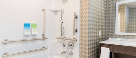 Un baño moderno con ducha a nivel, barras de apoyo, tocador con espejo y toallero.