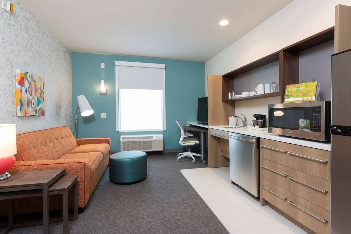 A compact living space with a kitchenette, a sofa, a desk, and a chair.