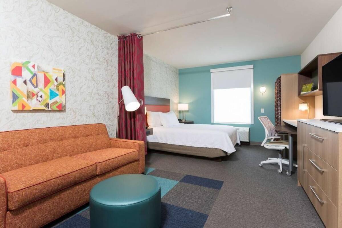 A hotel room with a sofa, bed, desk, chair, and a TV.