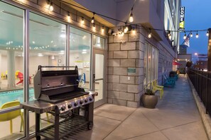 Un patio al aire libre con una parrilla, una zona de estar y una piscina de fondo.