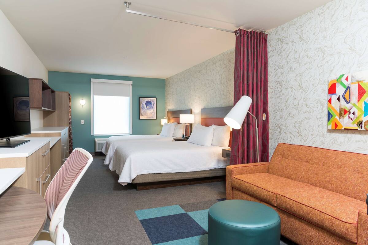 A hotel room with a bed, a sofa, a desk with a chair, a TV, and a window with curtains.