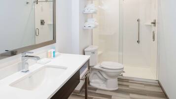 Un baño moderno con ducha envuelta en vidrio, un lavabo blanco con espejo y un inodoro.
