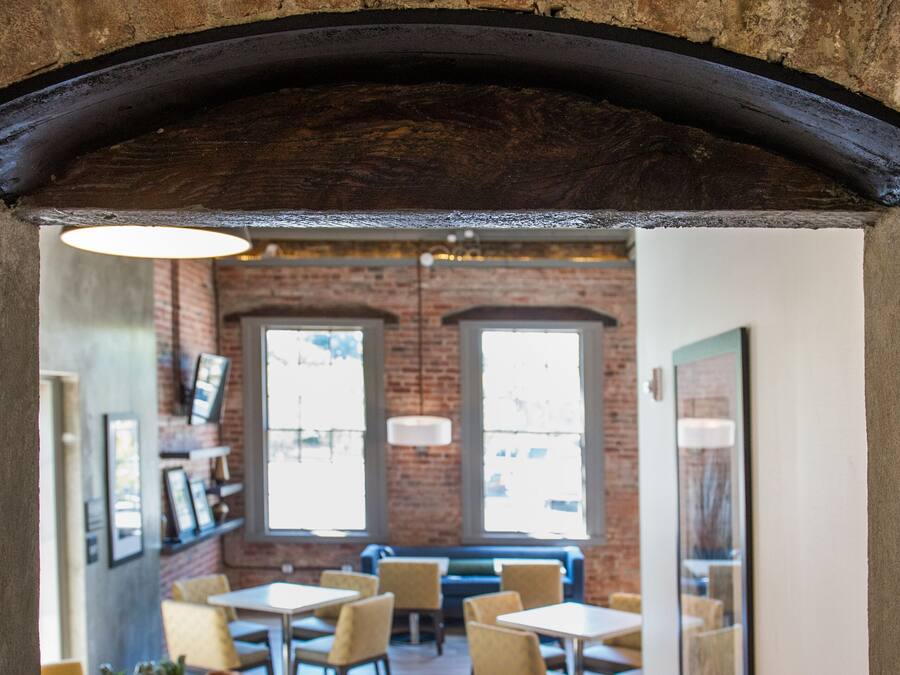 Een interieur van een restaurant met bakstenen muren, houten vloeren en een combinatie van gele en witte tafels en stoelen.