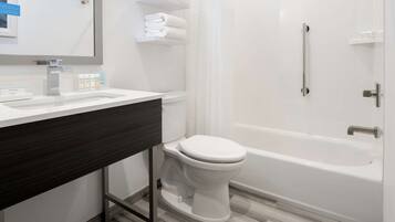 A modern bathroom with a white sink, toilet, and bathtub. There are white towels on a shelf and a mirror above the sink.