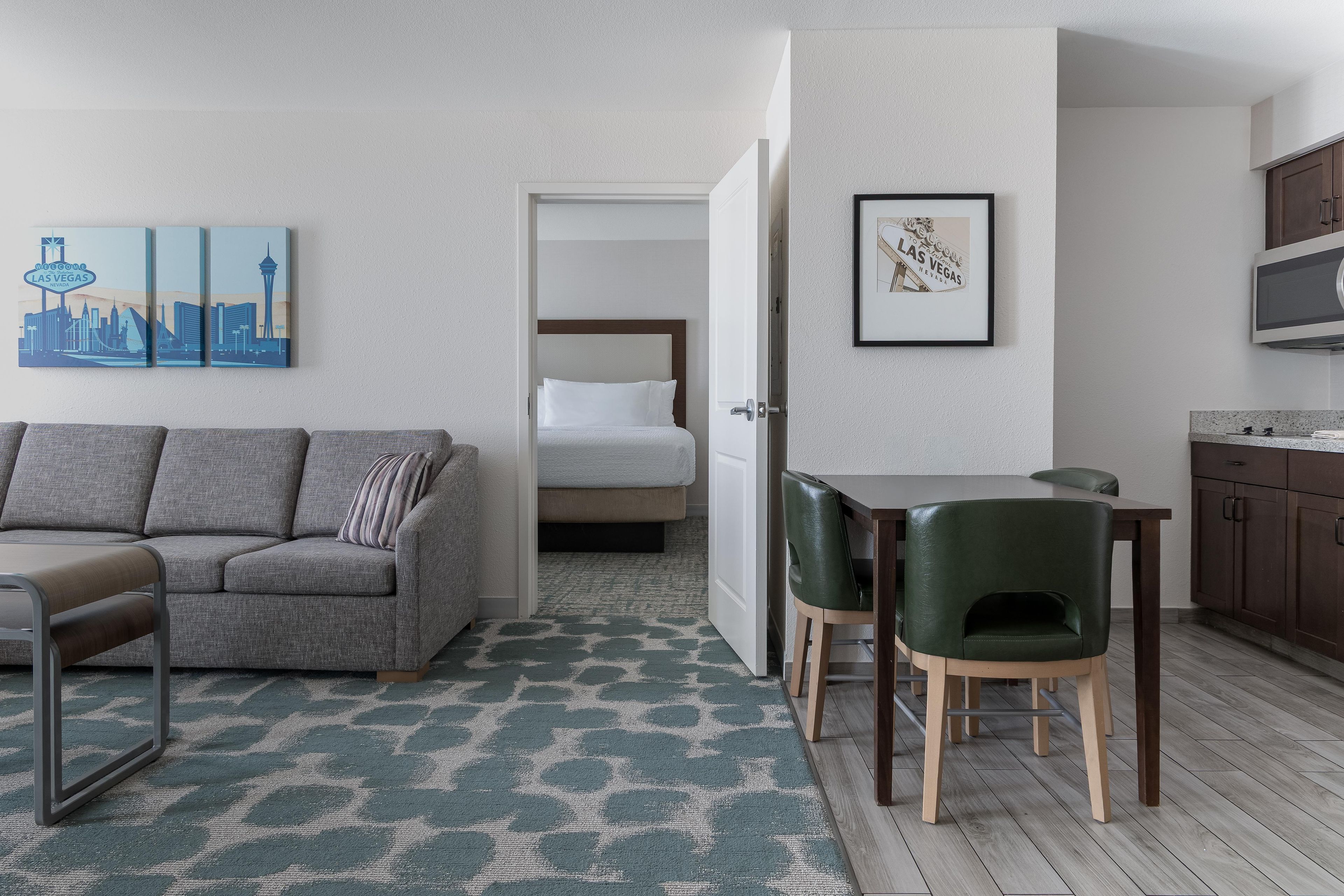 Ein Hotelzimmer mit grauem Sofa, einem grünen Sessel, einem Bett, einem kleinen Tisch und einer Mikrowelle.