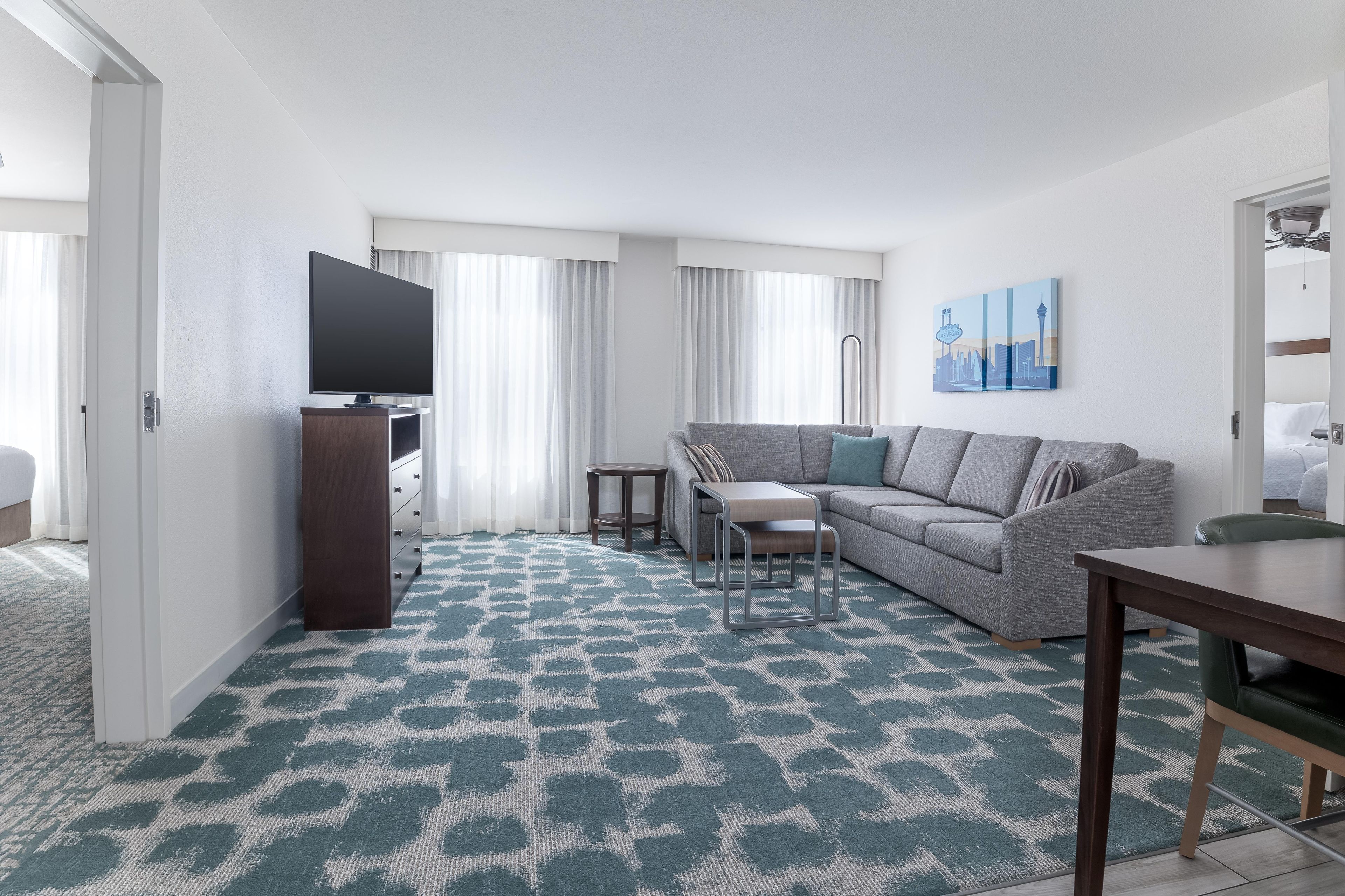 Habitación de hotel con sofá, una mesita, televisión y un cuadro en la pared.