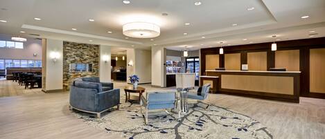 A spacious lobby with a reception desk, seating area with sofas and chairs, a stone accent wall, and a large window providing natural light.