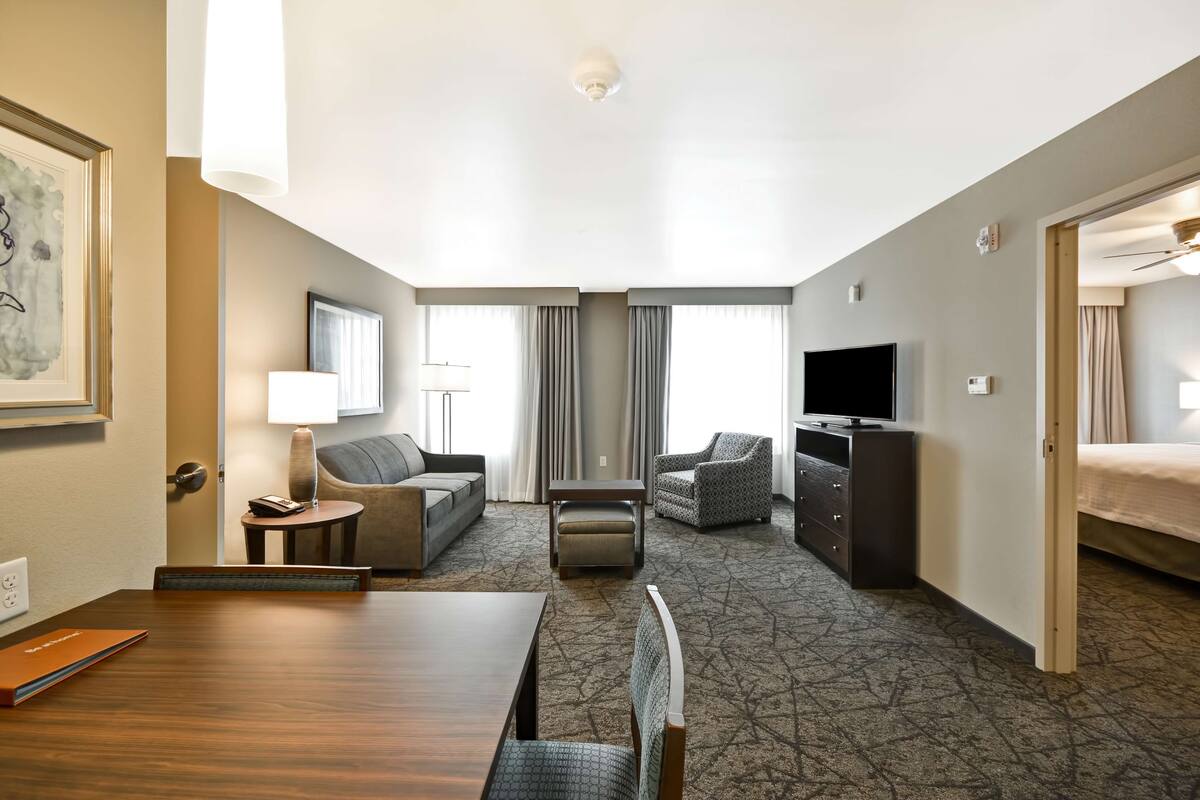 Habitación de hotel con mesa de comedor, sofá, sillón, televisor y cama.