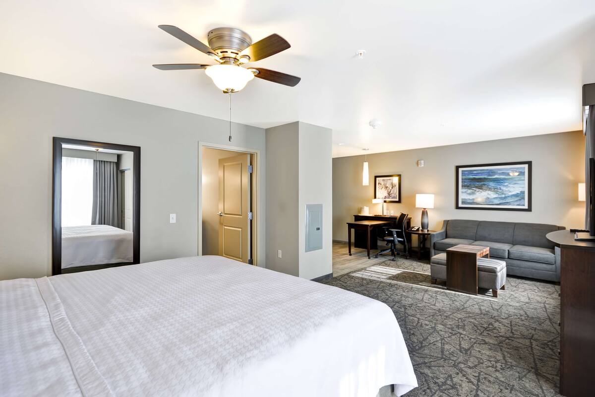Habitación de hotel con cama, escritorio, sofá y ventilador de techo.