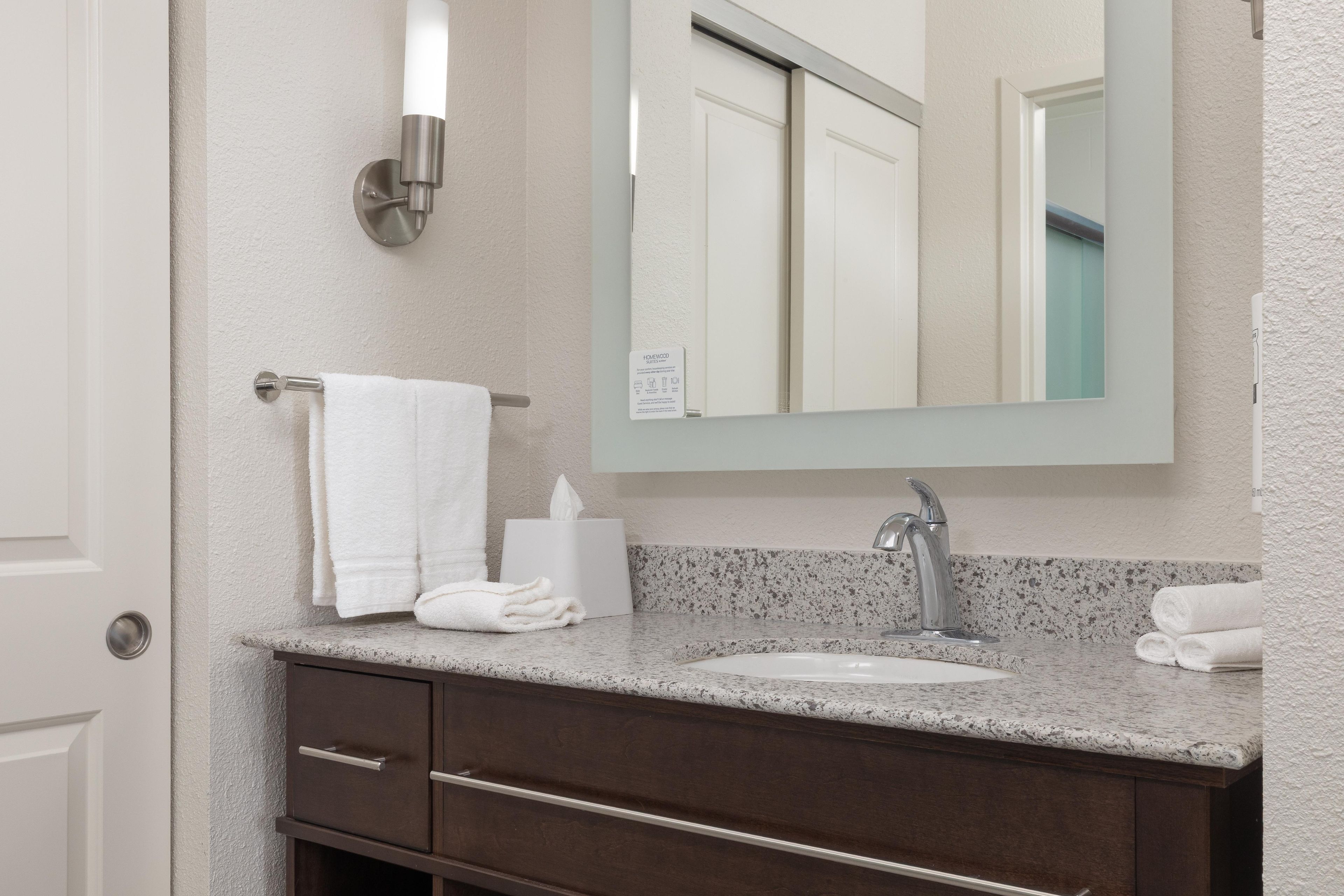 Un bagno con lavandino, specchio, porta asciugamani e distributore di fazzoletti.
